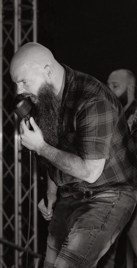 Bärtiger Musiker mit Mikrophon auf einer Bühne, während er performt.