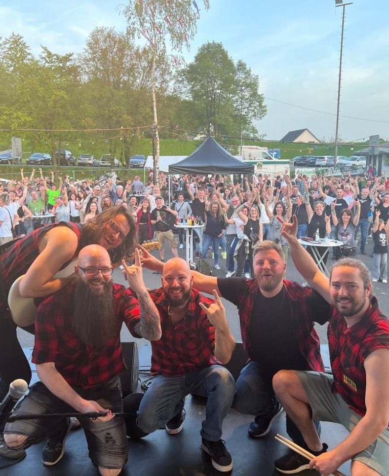 Eine Band posiert mit Fans vor einer großen Menschenmenge bei einem Konzert.