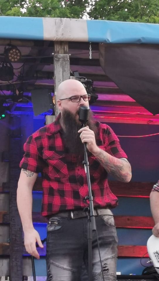 Mann mit Bart und Brille trägt ein kariertes Hemd und singt ins Mikrofon.