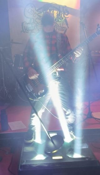 Ein Bassist auf der Bühne, umgeben von hellen Lichtern und Rauch.