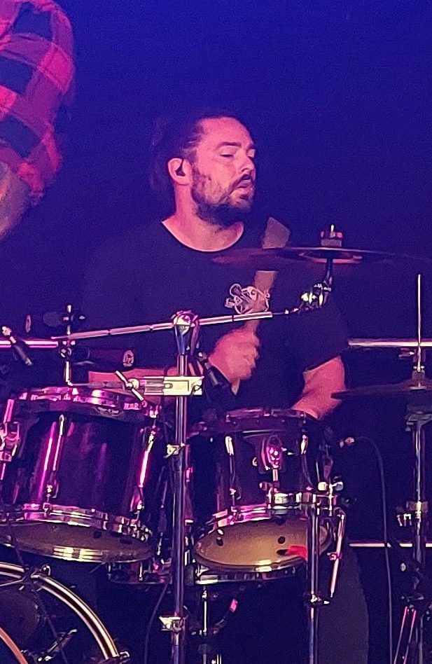 Ein Schlagzeuger spielt aktiv, mit Stöcken in der Hand und konzentriertem Gesichtsausdruck.