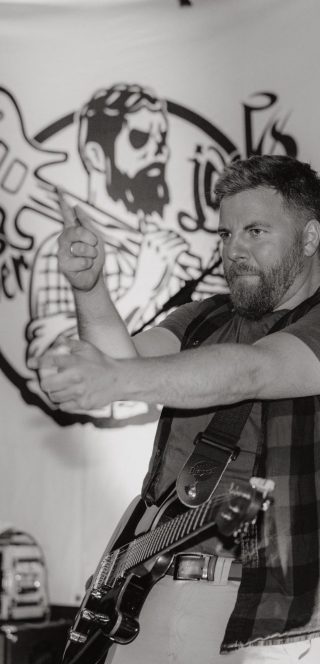 Ein Musiker mit Bart spielt Gitarre und gestikuliert auf einer Bühne.