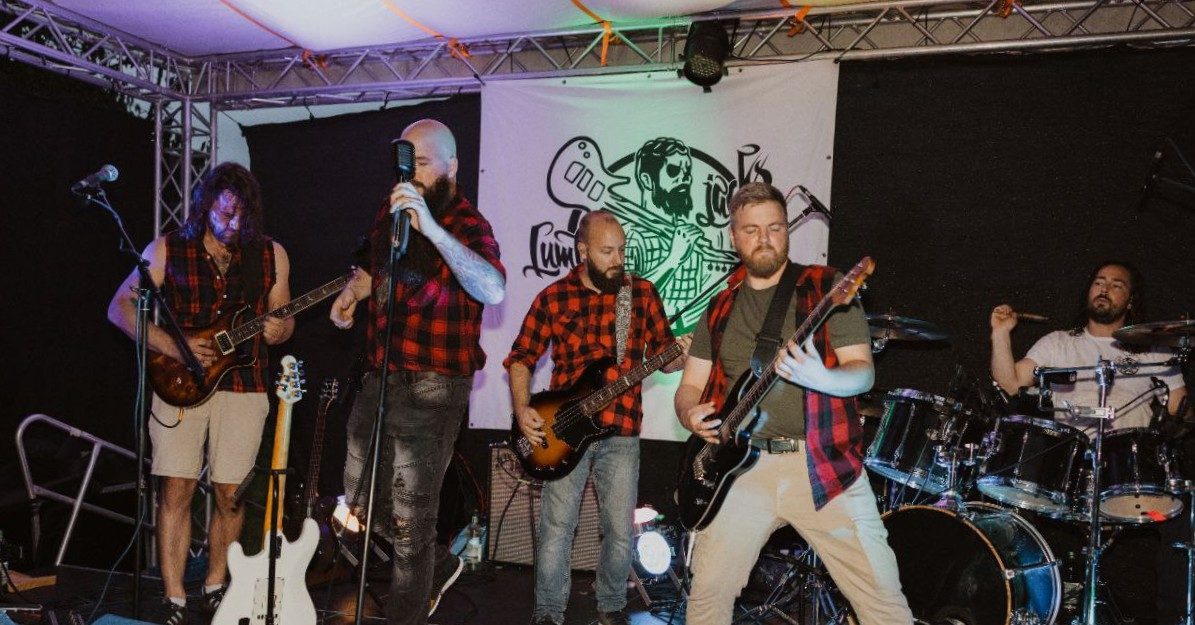 Rockband auf der Bühne mit Gitarren, Drums und roten Holzfällerhemden. 